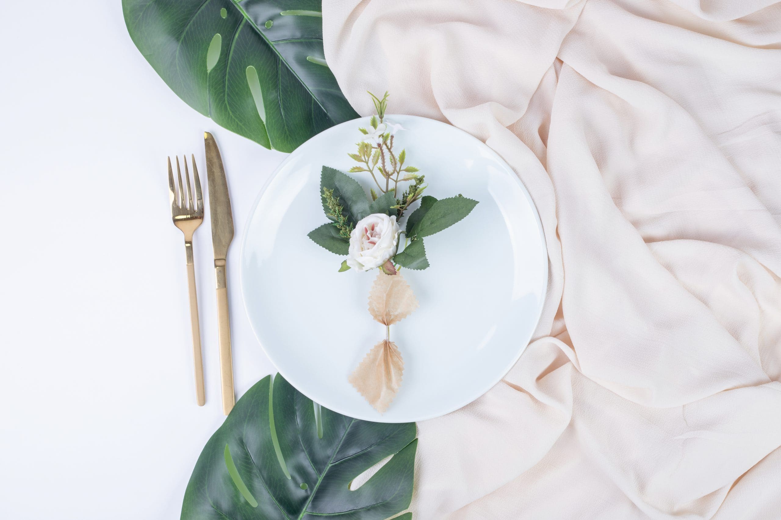 Single rose on white plate with fake leaves and tablecloth
